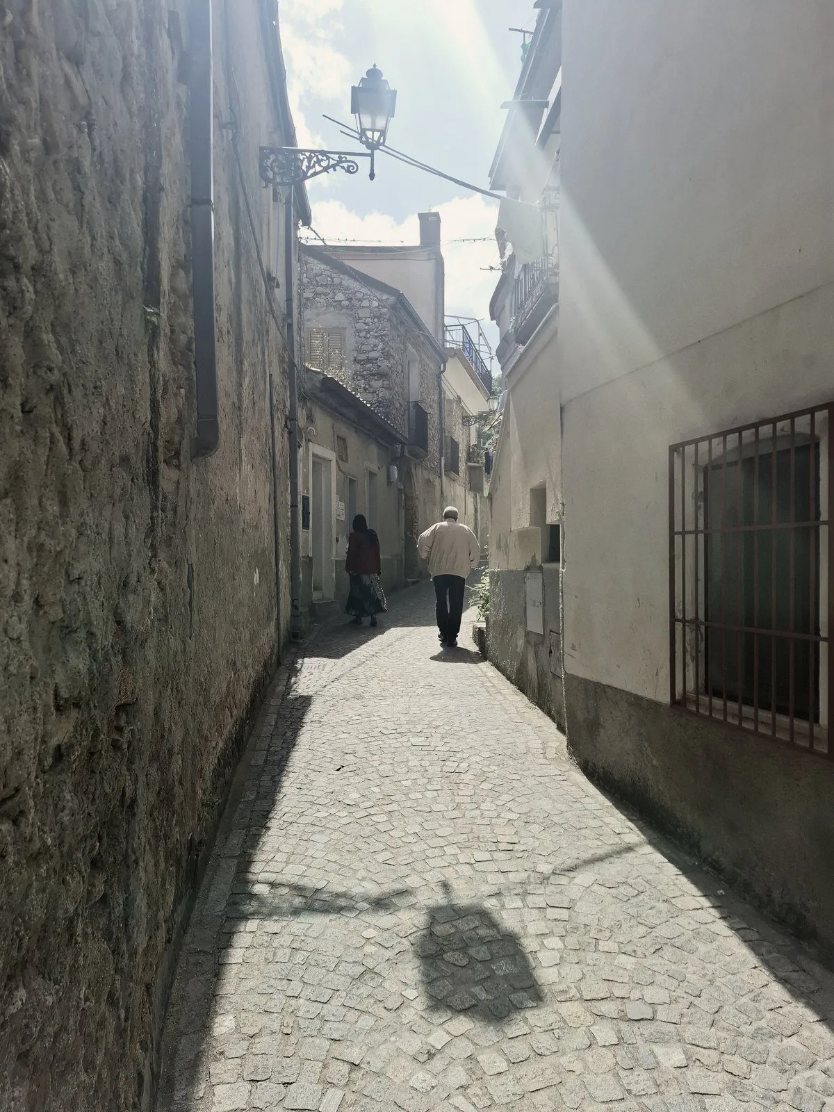 Ruelle ensoleillée à contre-jour, deux passants de dos